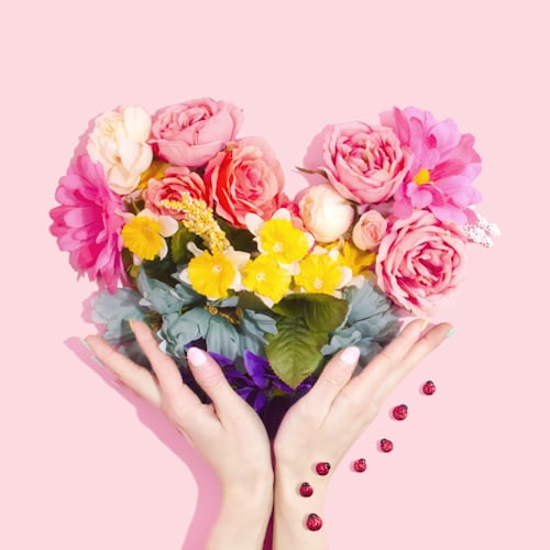 Colorful heart-shaped bouquet of fresh roses and mixed flowers held in hands